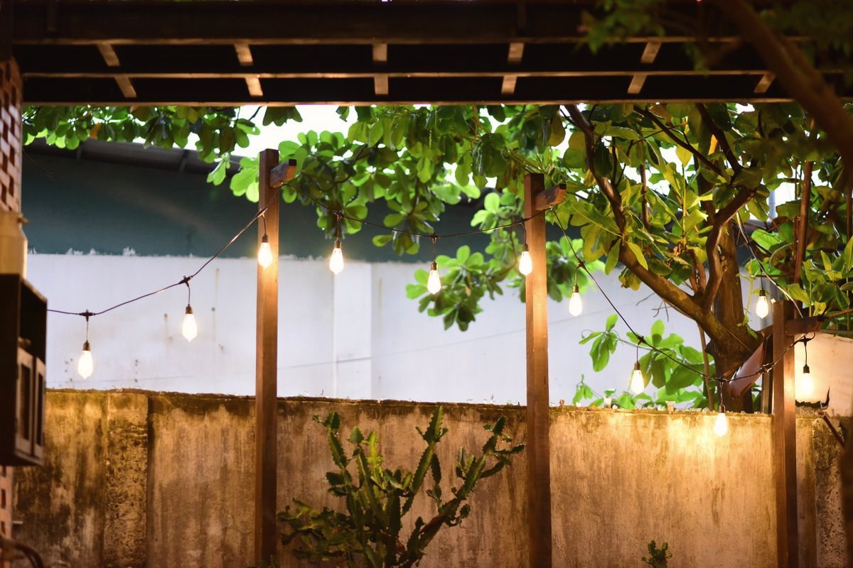 A pergola patio strung with lights under a leafy tree in the evening